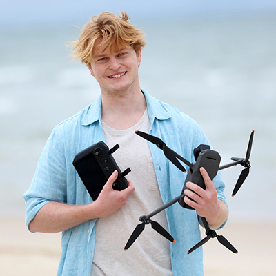 A man on a beach holding a drone and a remote control for it